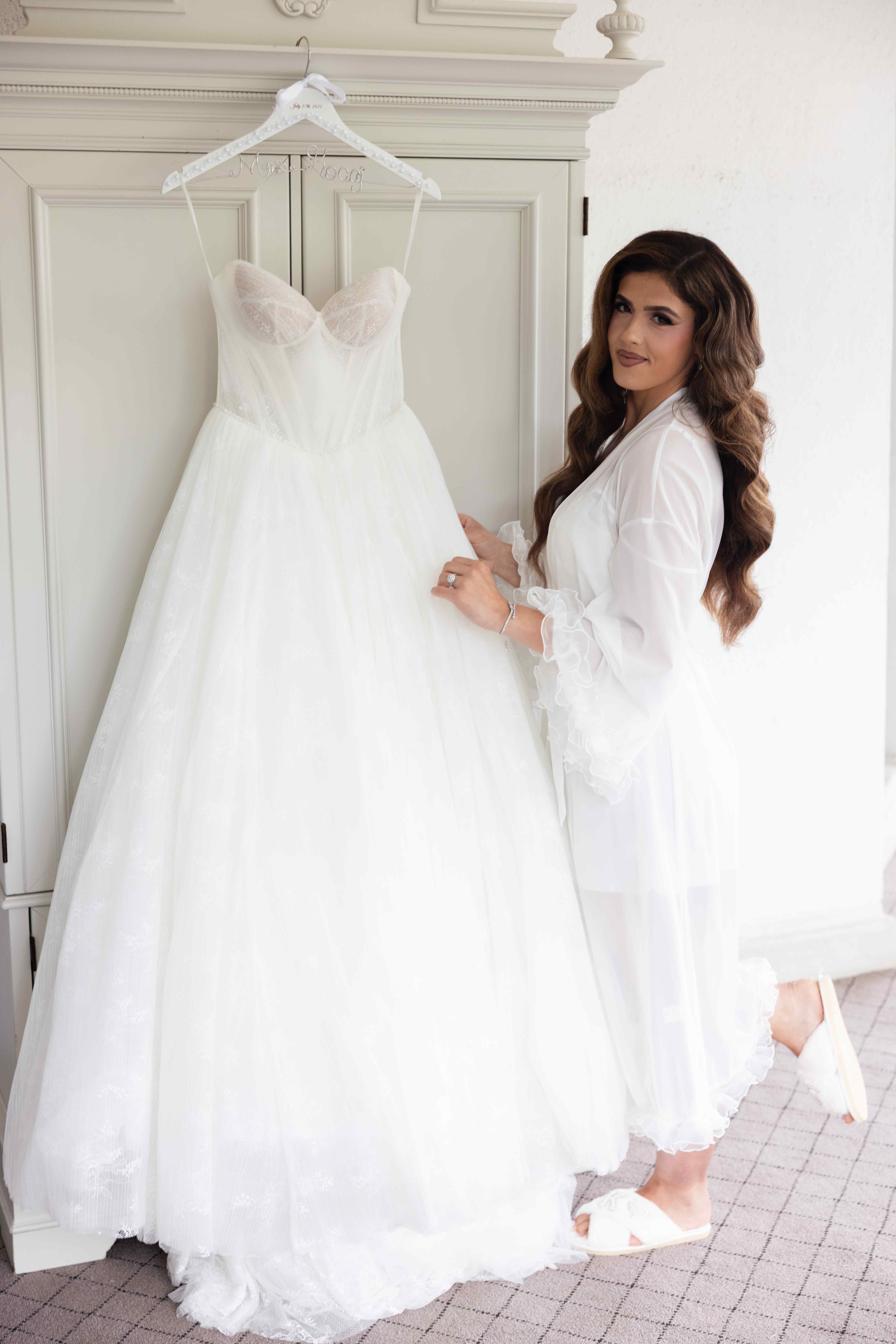 Bride getting ready with elegant wedding dress hanging in preparation